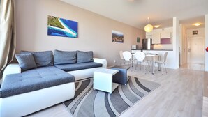 A modern living room with a sectional sofa, a dining area with a table and chairs, and a kitchen in the background. - BRETIA apartments & more (Sutivan)