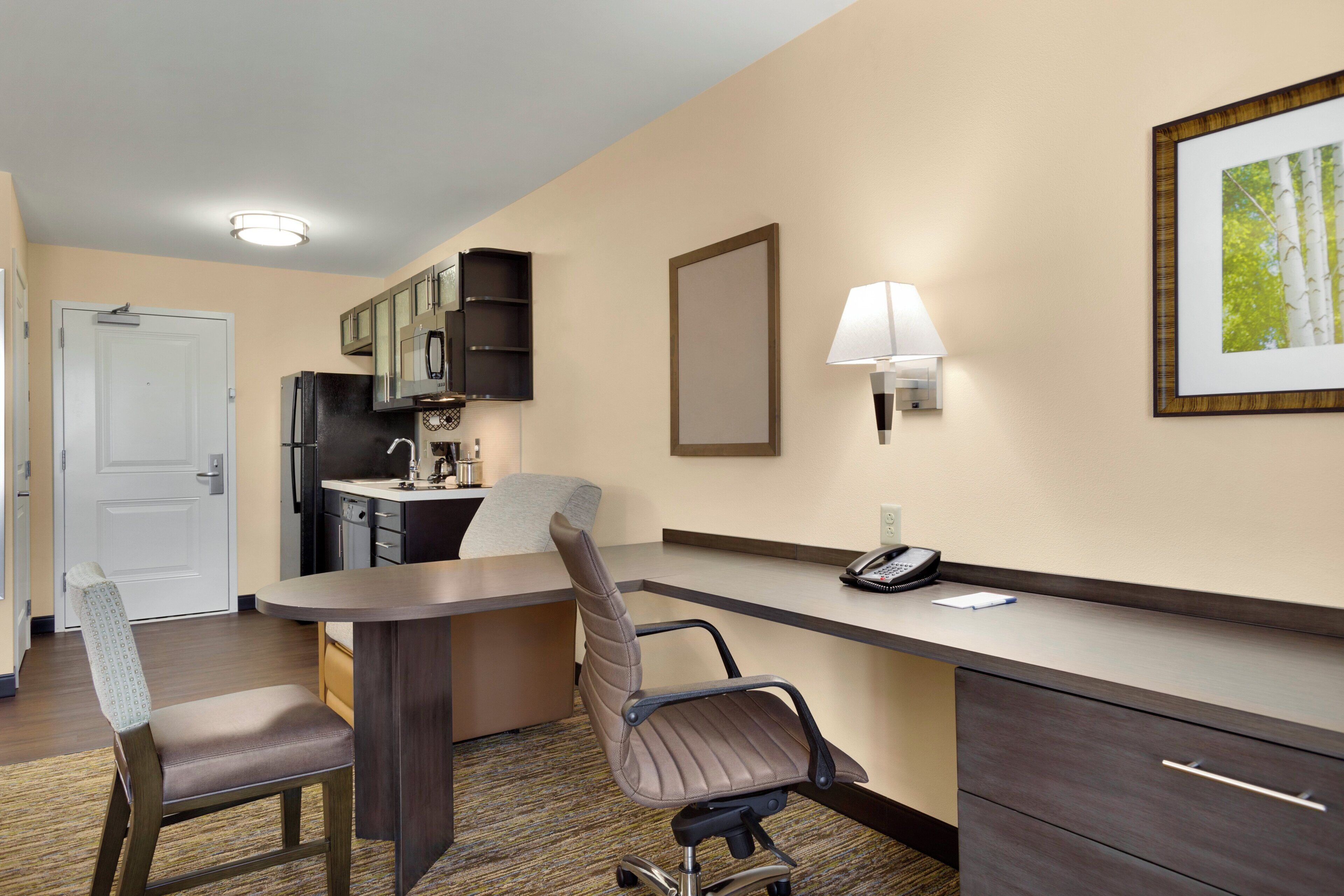 Quarto de hotel com cozinha compacta, escrivaninha com telefone, cadeira e cama.