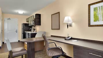Una habitación de hotel con kitchenette, un escritorio con teléfono, una silla y una cama.