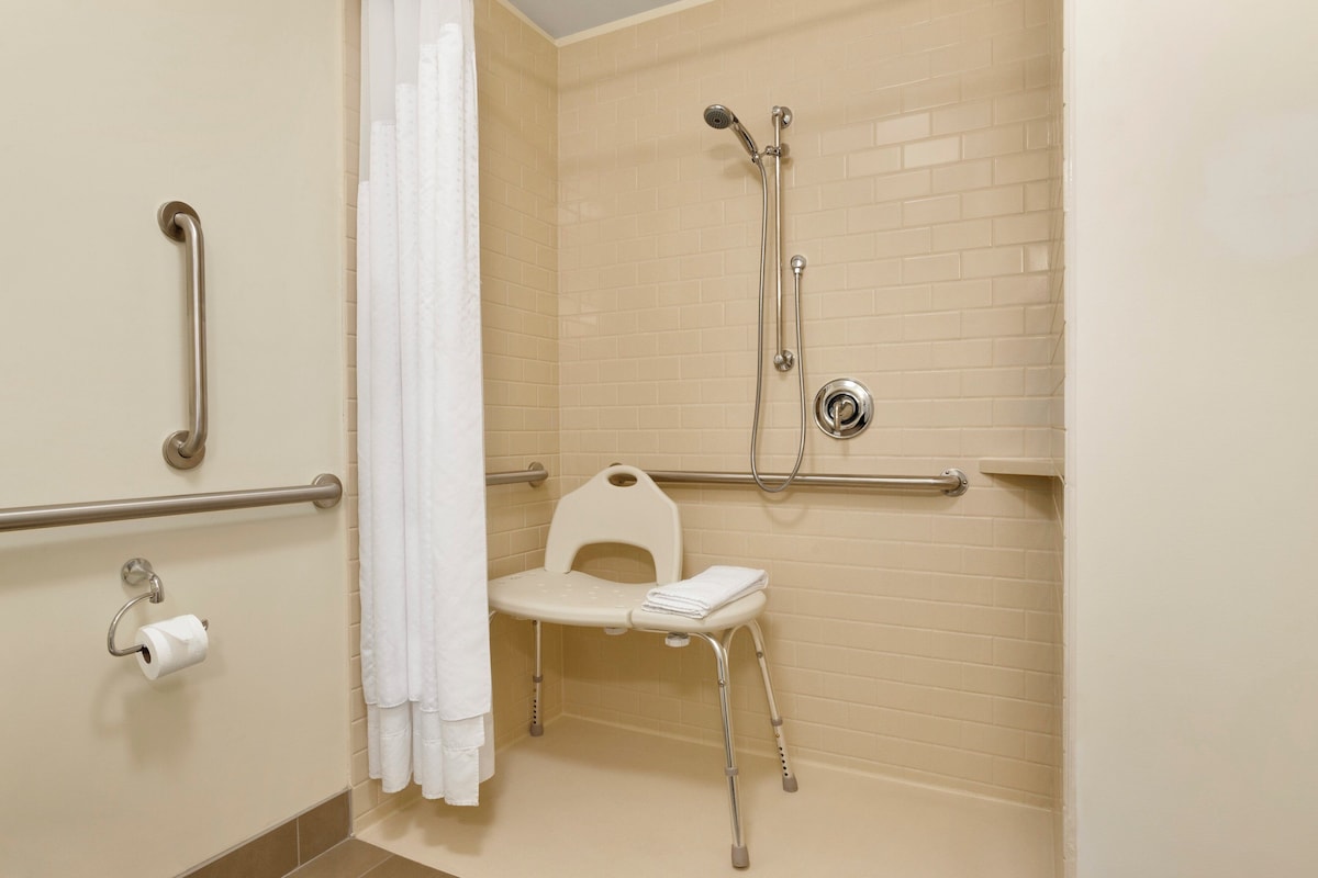 A handicap-accessible shower stall with grab bars, a wheelchair-accessible seat, and a toilet paper holder.
