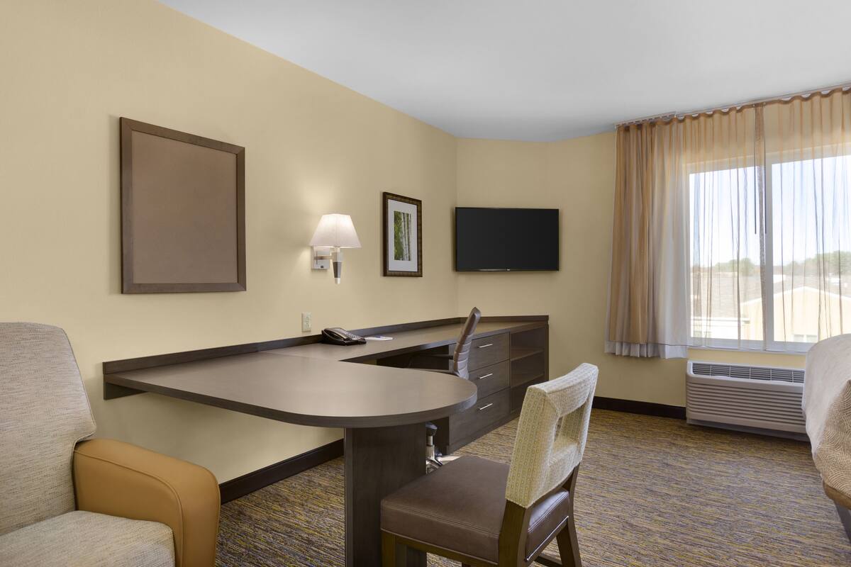 A hotel room with a desk, two chairs, a TV, a framed picture, and a window with curtains.