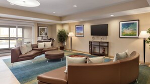A modern living room with a sectional sofa, a coffee table, and a flat-screen TV mounted on the wall. - Candlewood Suites Vestal - Binghamton by IHG (Vestal)
