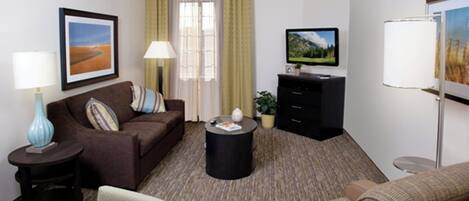 Een hotelkamer met een bruine bank, een kleinere fauteuil, een salontafel, een televisie op een standaard, een lamp en een schilderij aan de muur.