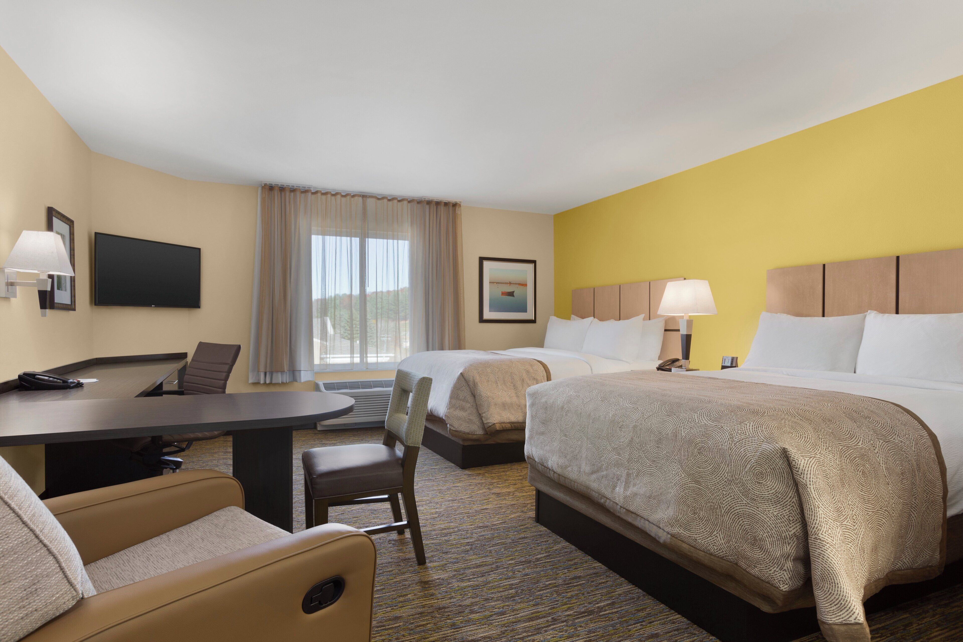 A hotel room with a desk, two beds, a chair, and a television.