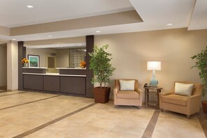 A reception area with a counter, two armchairs, a lamp, and a potted plant. - Candlewood Suites Vestal - Binghamton by IHG (Vestal)