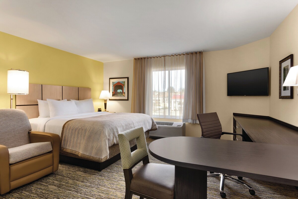 A hotel room with a bed, a desk, a chair, a TV, and a window with curtains.