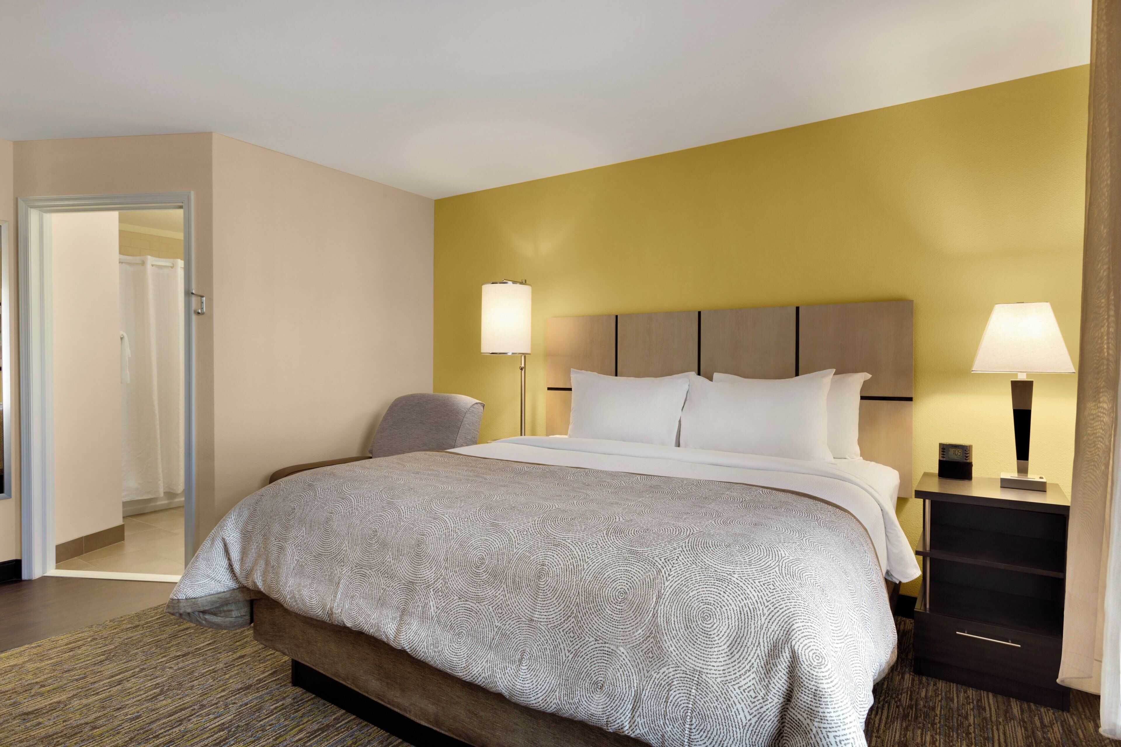 Ein Hotelzimmer mit einem Bett, Nachttischen, einem Sessel und einer Tür zu einem Badezimmer.