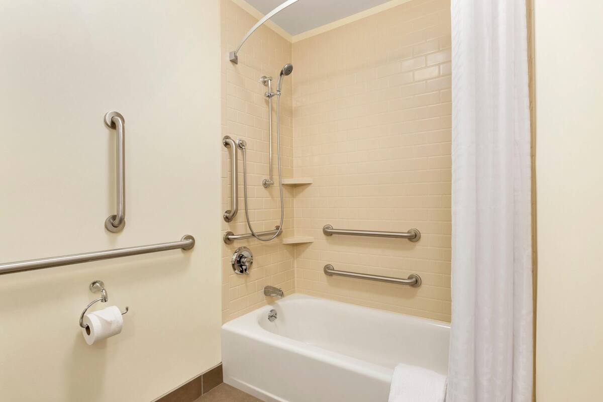A bathroom with a white bathtub, a shower with grab bars, and a toilet with a paper towel holder.