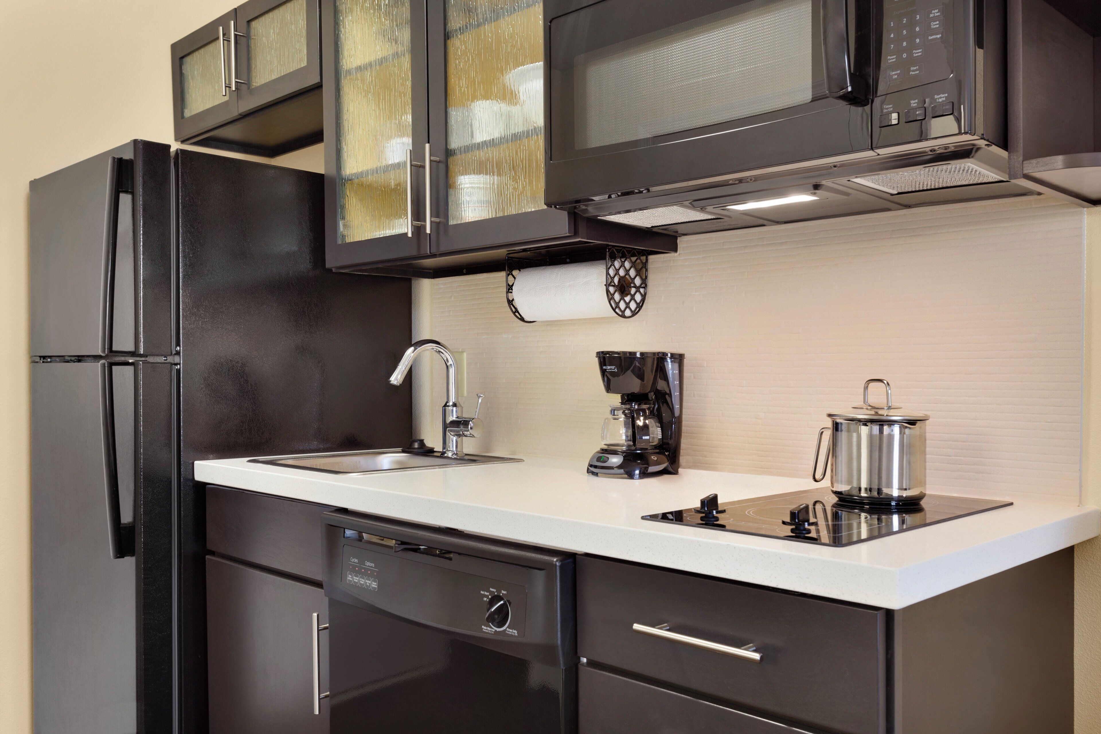A modern kitchen with a black refrigerator, a microwave, a coffee maker, and a pot on the stove.