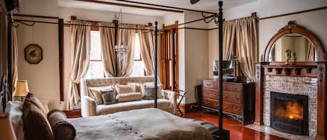 Un dormitorio con cama con dosel, chimenea, televisor y candelabro.