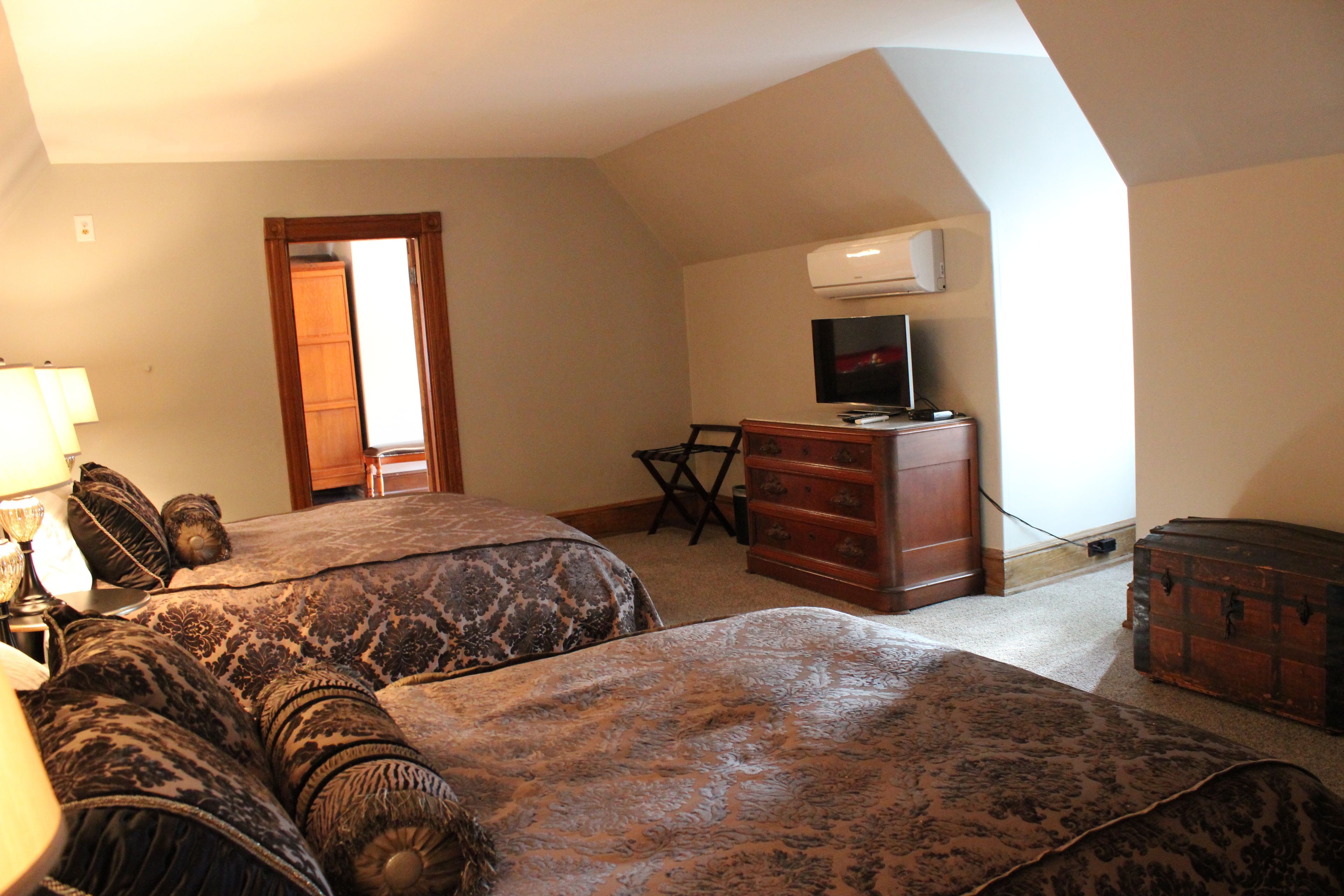 A bedroom with two beds, a dresser, a desk, and an air conditioning unit.