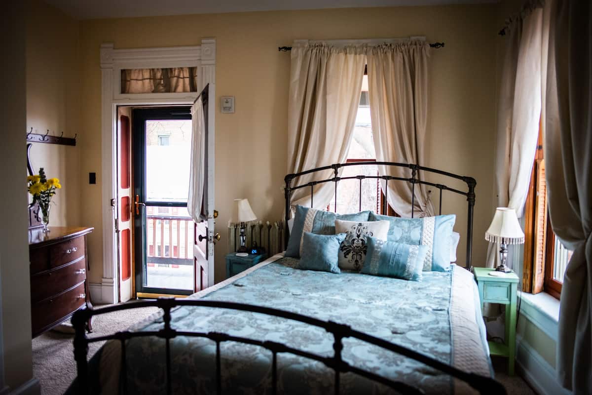 Une chambre à coucher comprenant un lit, des tables de chevet, une commode et une porte donnant sur l’extérieur.