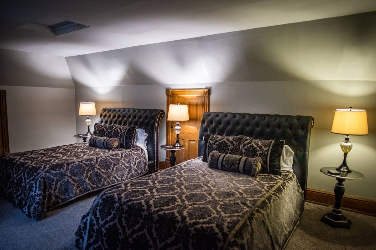Une chambre d’hôtel avec deux lits, chacun recouvert d’une couvre-lit à motifs, une porte en bois et deux lampes de chevet.