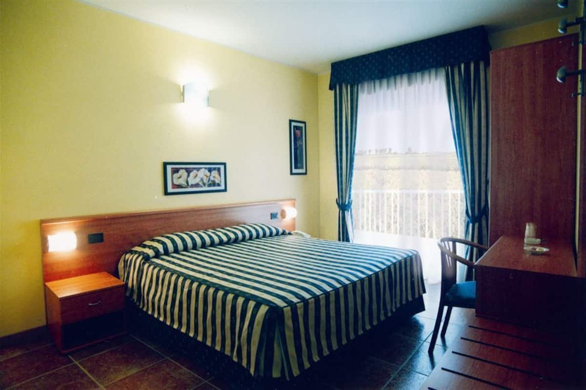 A hotel room with a bed, a nightstand, a desk, and a chair.