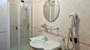 A bathroom with a glass shower enclosure, a white sink, a round mirror, and a hairdryer on the wall. - Hotel Blue Ribbon (Vercelli)