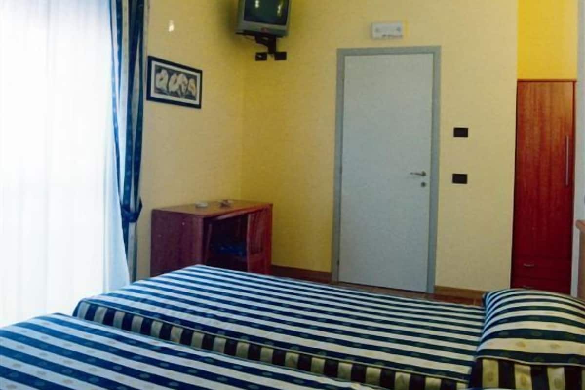 A hotel room with two beds, a television on the wall, a door, and a small table.