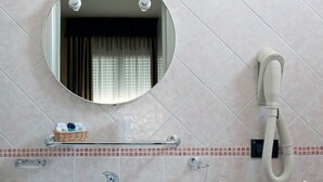 A bathroom with a round mirror, a towel rack, a hand dryer, and a small basket with toiletries. - Hotel Blue Ribbon (Vercelli)