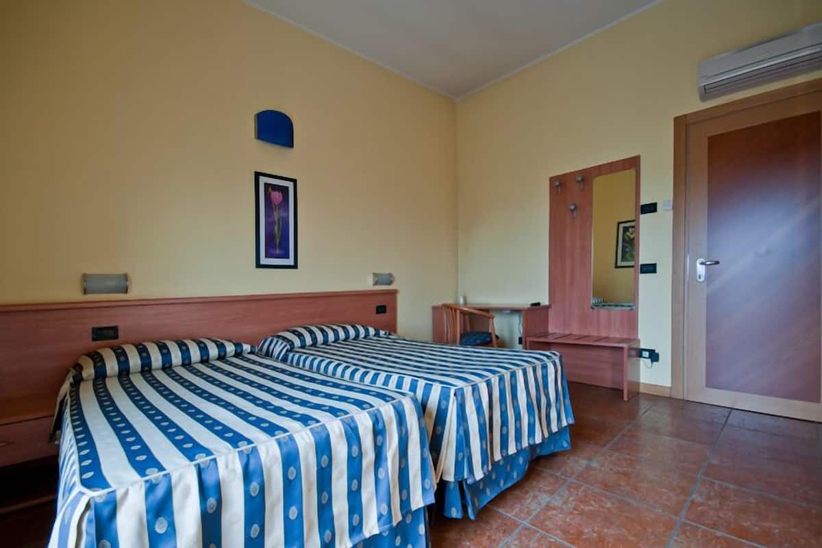 A room with two beds, a desk, a chair, a mirror, and a door.