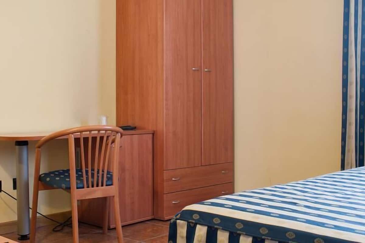 A bedroom with a bed, a wooden wardrobe, a desk with a chair, and a striped curtain.