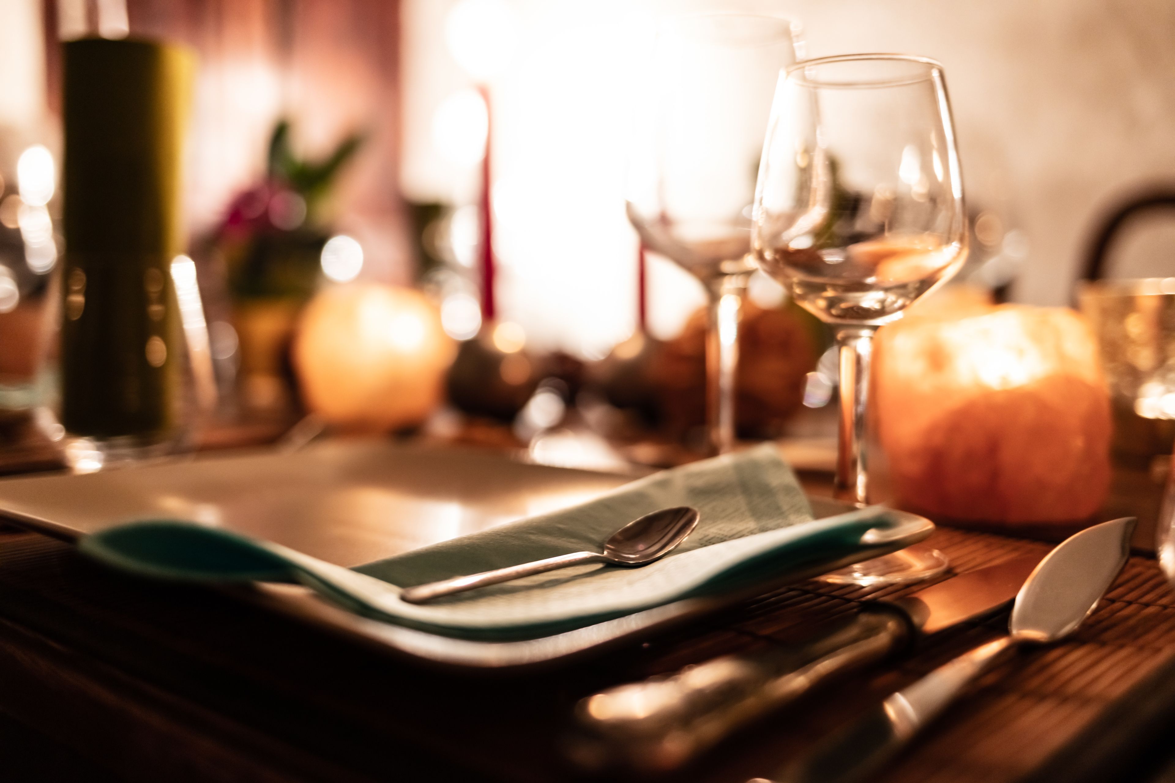A dining table set with a green placemat, a spoon, a knife, and a glass of white wine.