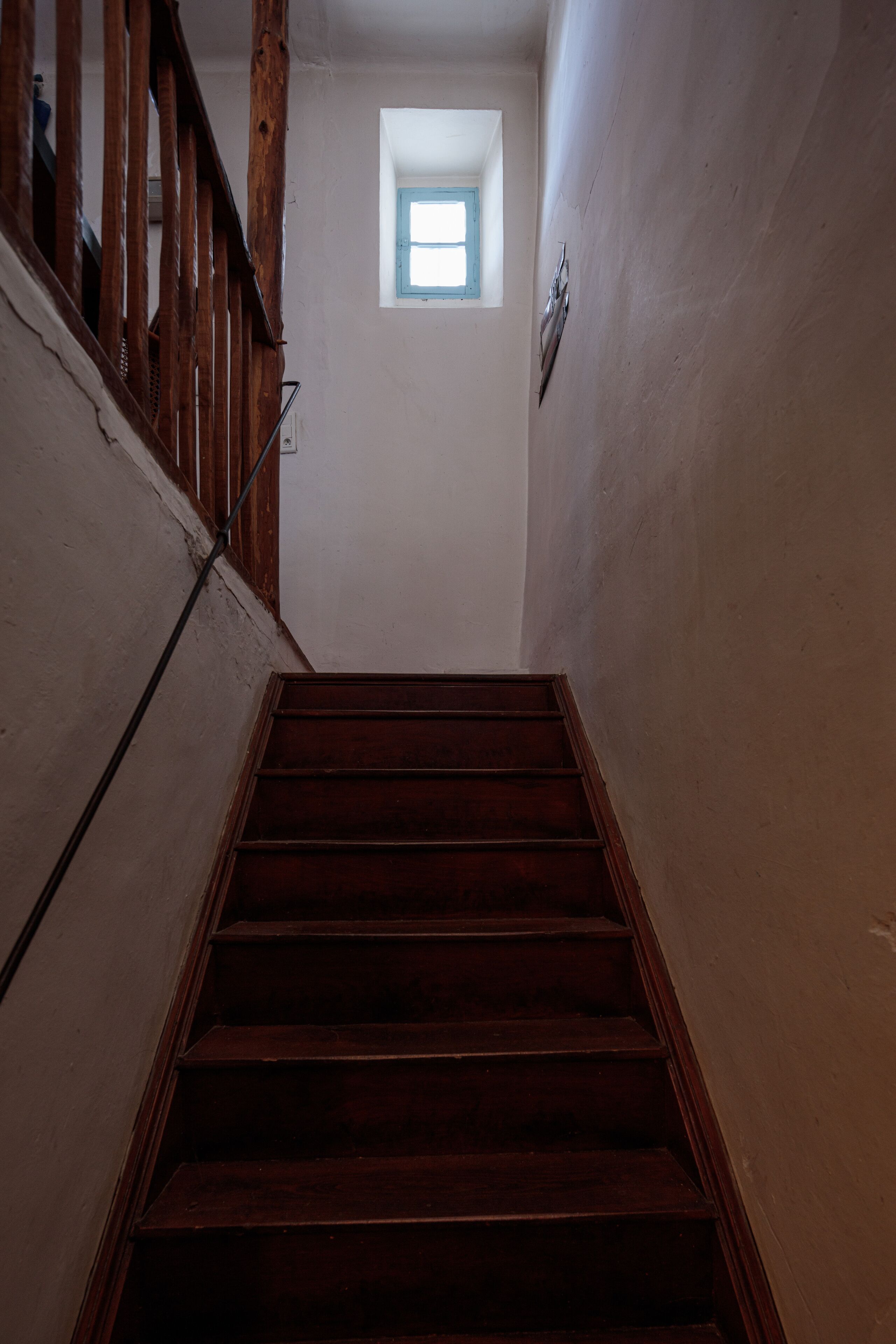 Una escalera de madera que lleva a una habitación con un ventanal pequeño.