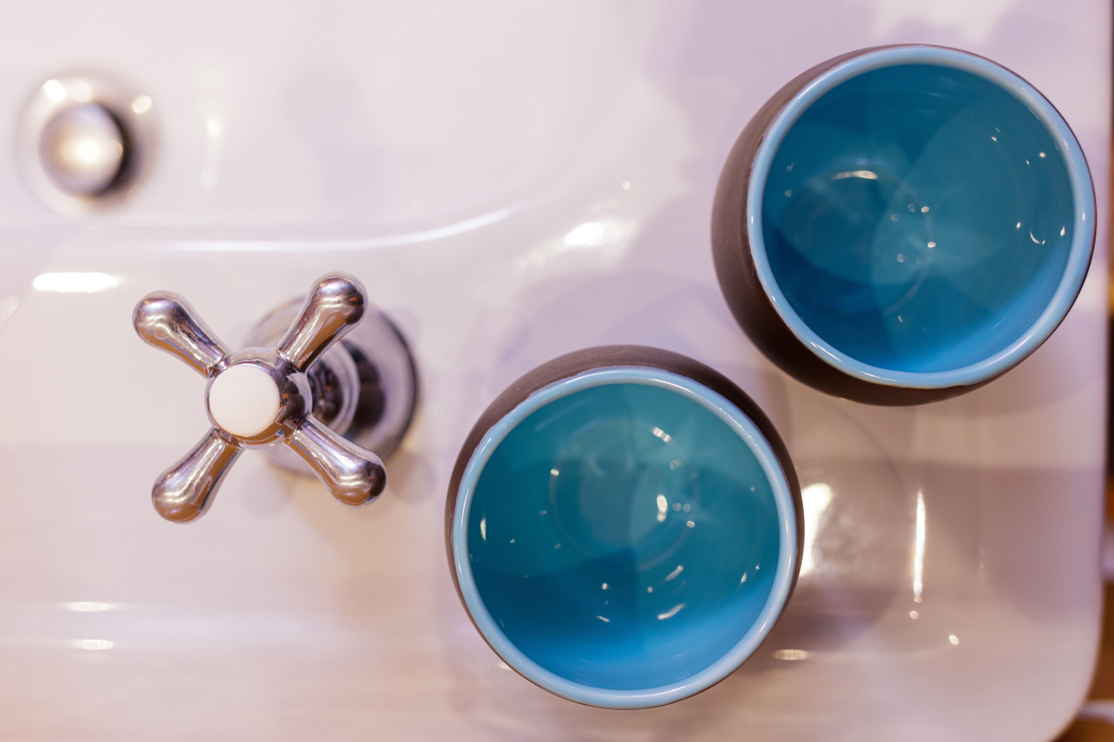 A bathroom with a white sink and two blue cups on it.