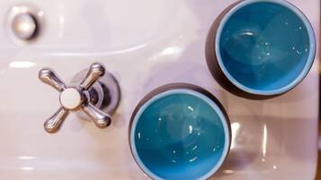 A bathroom with a white sink and two blue cups on it.