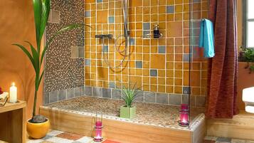 Un baño con piso a cuadros, ducha con puerta de vidrio, pared con azulejos y una planta en maceta.
