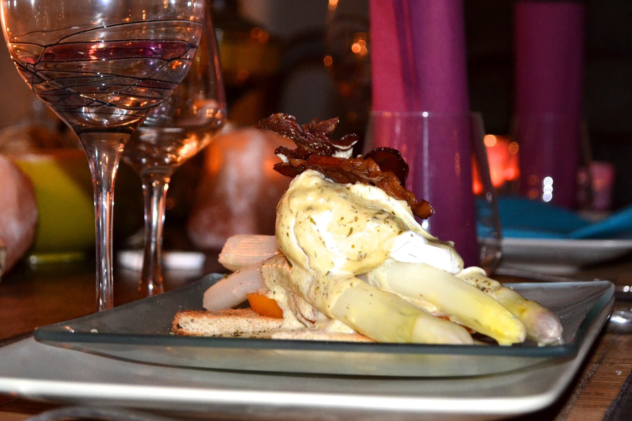 A glass of red wine and a plate with a dish of food, including a piece of meat and vegetables, on a table.