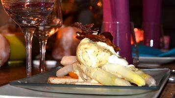 A glass of red wine and a plate with a dish of food, including a piece of meat and vegetables, on a table.