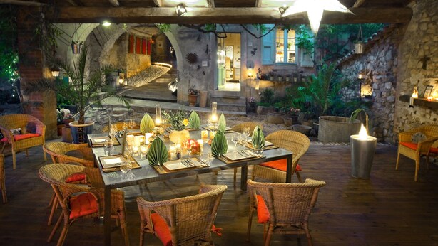 An outdoor dining area with wicker chairs, a table set for a meal, and a stone wall in the background.