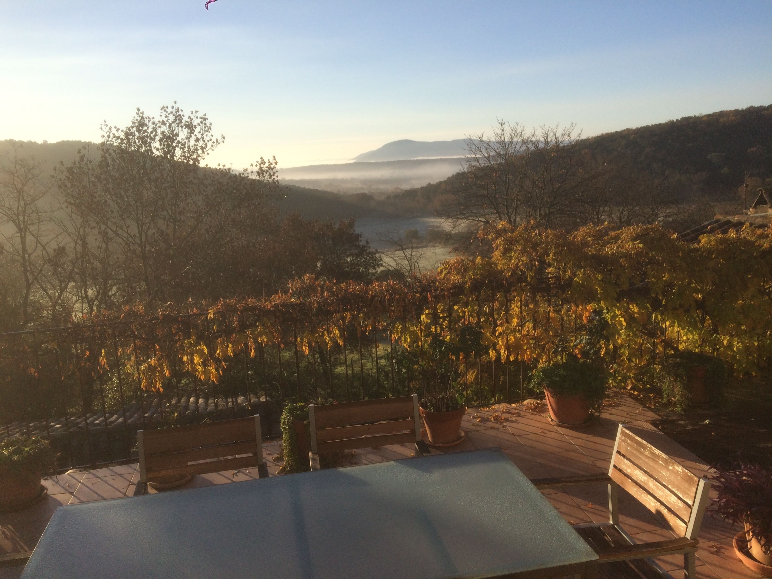 Una mesa y bancos en una terraza con vistas a un valle con árboles y una lejana cadena montañosa.