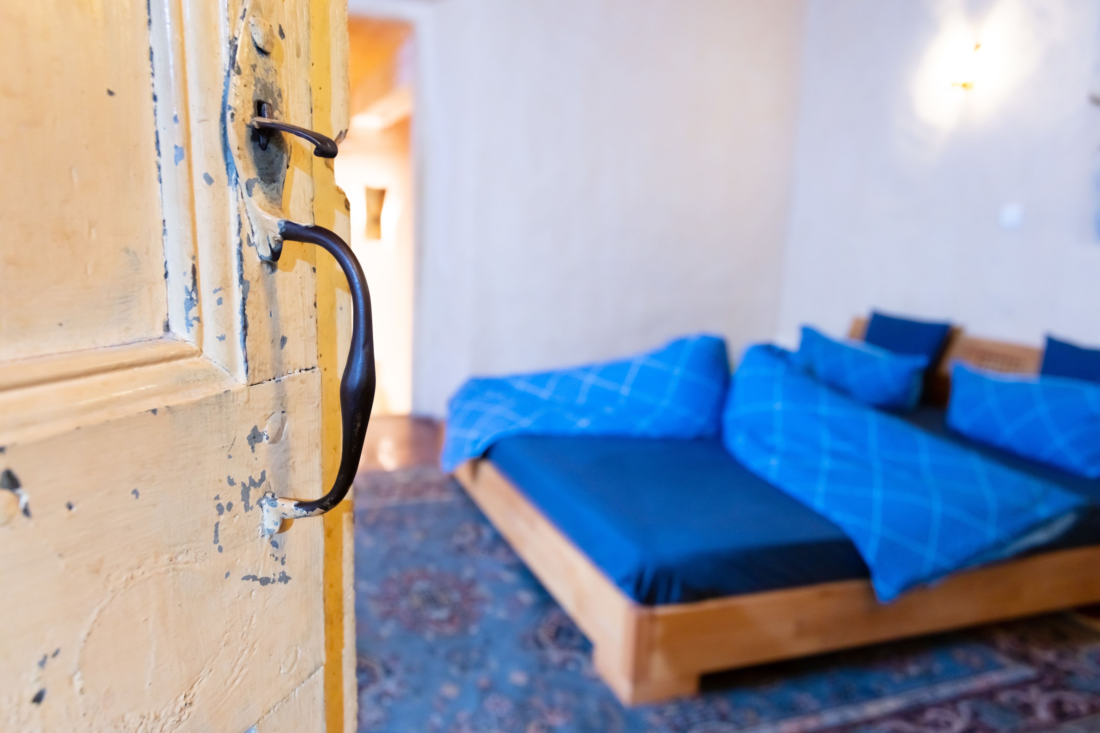 A room with a wooden bed, blue bedding, and a patterned carpet.
