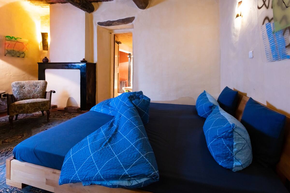 Une chambre à coucher avec un lit en bois, une literie bleue, une chaise et une cheminée.