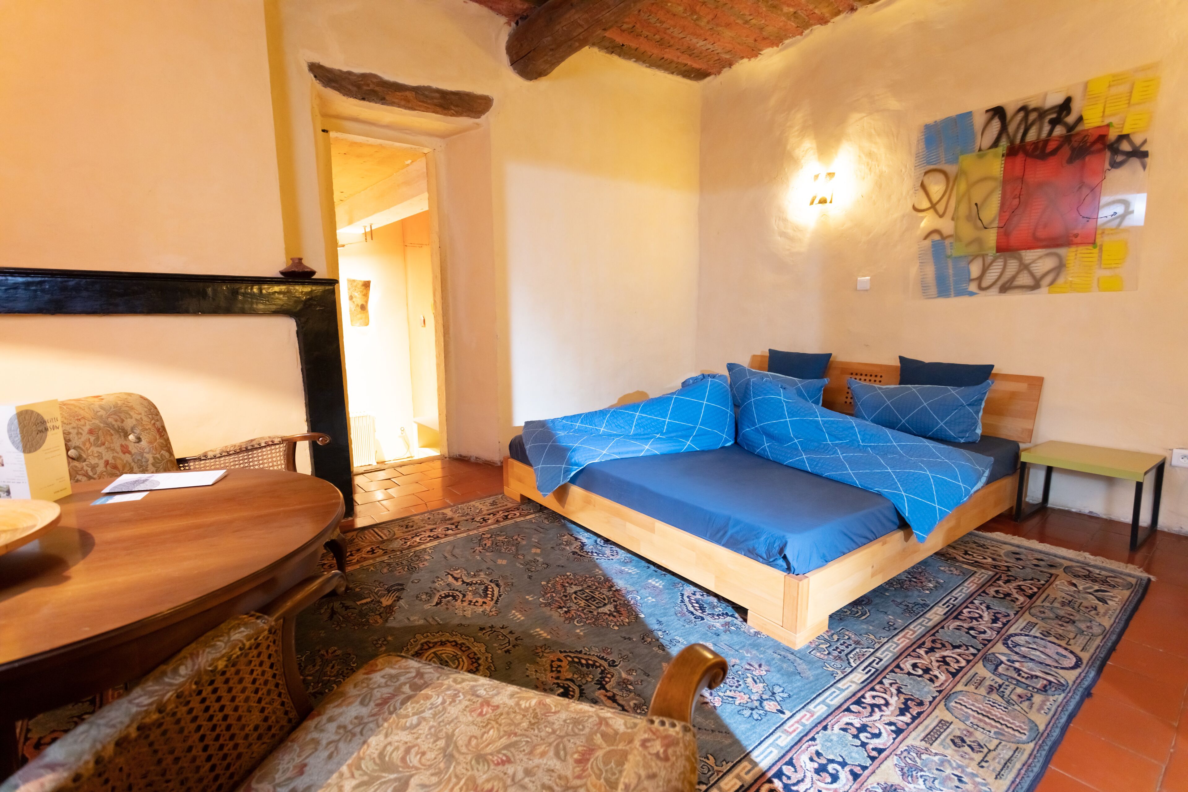 Une chambre à coucher avec un lit en bois, une literie bleue, un tapis à motifs, une table en bois et une chaise.