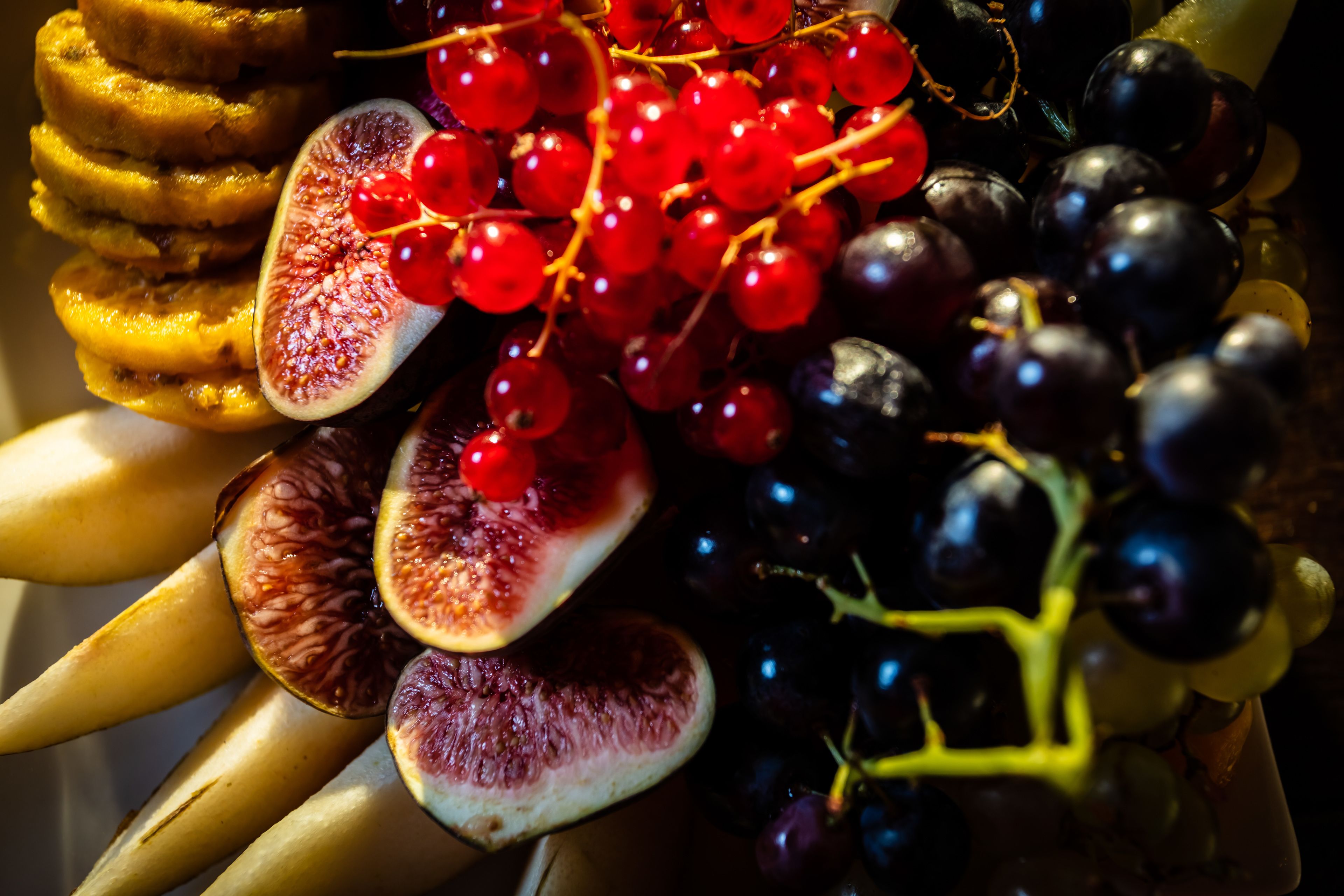 A fruit platter with sliced bananas, figs, red currants, and grapes.
