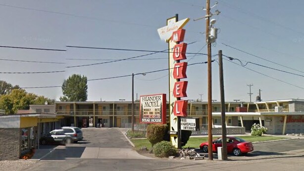 Un motel con un letrero llamativo, un estacionamiento y un edificio de techo plano.