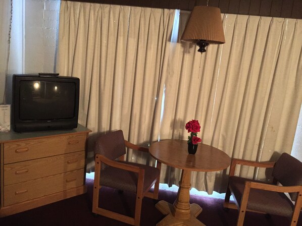 Una habitación con un mueble de televisión de madera, una pequeña mesa con un florero y dos sillas.