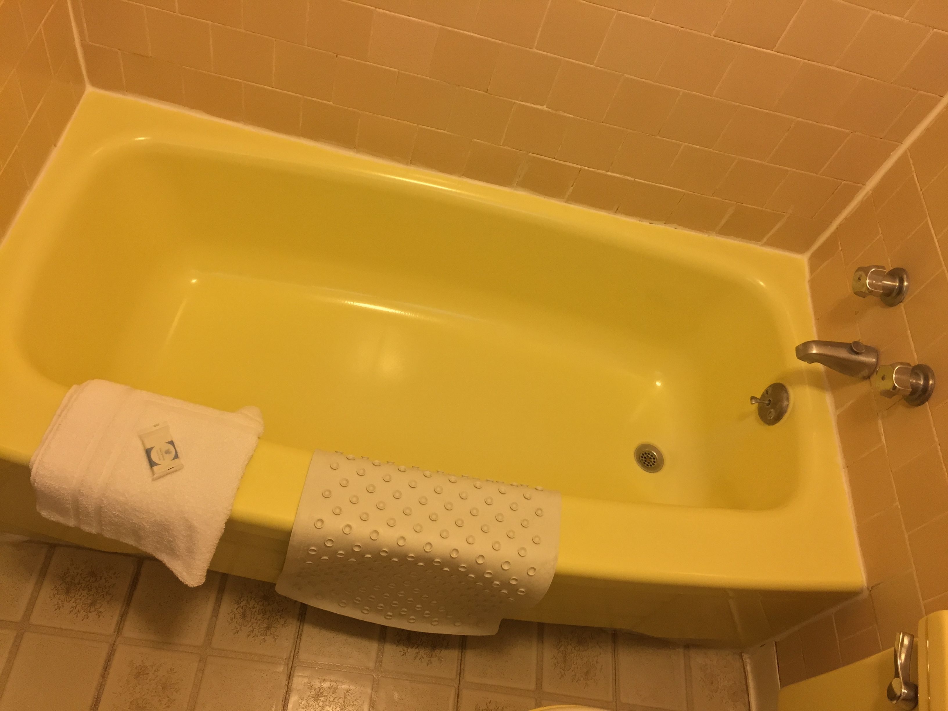 A yellow bathtub with a white towel and a textured bath mat.