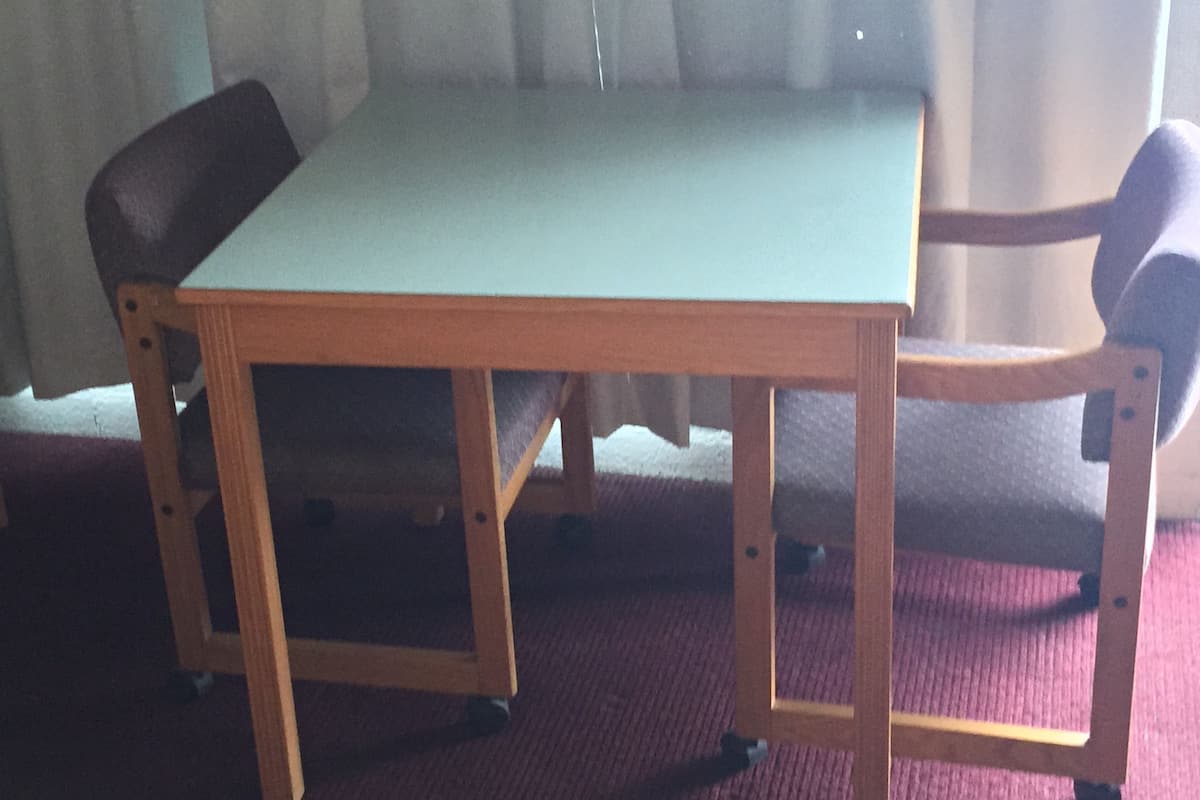 A wooden table with a light green top, surrounded by four chairs with dark upholstery.