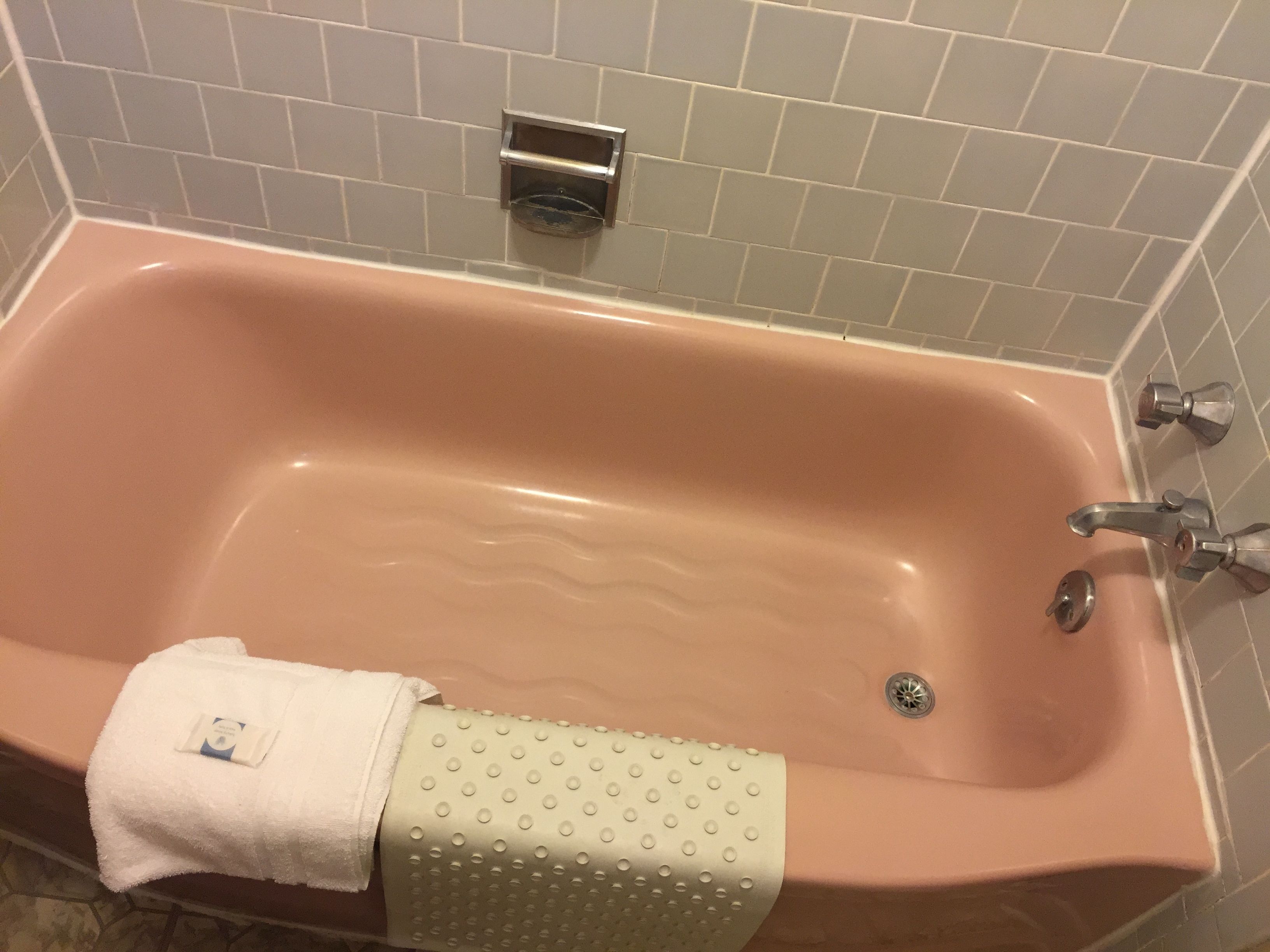 A pink bathtub with a white towel and a green towel with a pattern.
