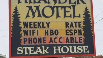 Señal del motel Hilander anunciando tarifas semanales, WiFi, HBO, ESPN, disponibilidad telefónica y un restaurante de carne.