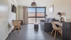 Habitación de hotel moderna con zona de comedor, sofá, escritorio y ventana grande con vista a la ciudad.