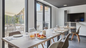 Un comedor moderno con ventanas amplias, un televisor de pantalla plana y una mesa lista para el desayuno.