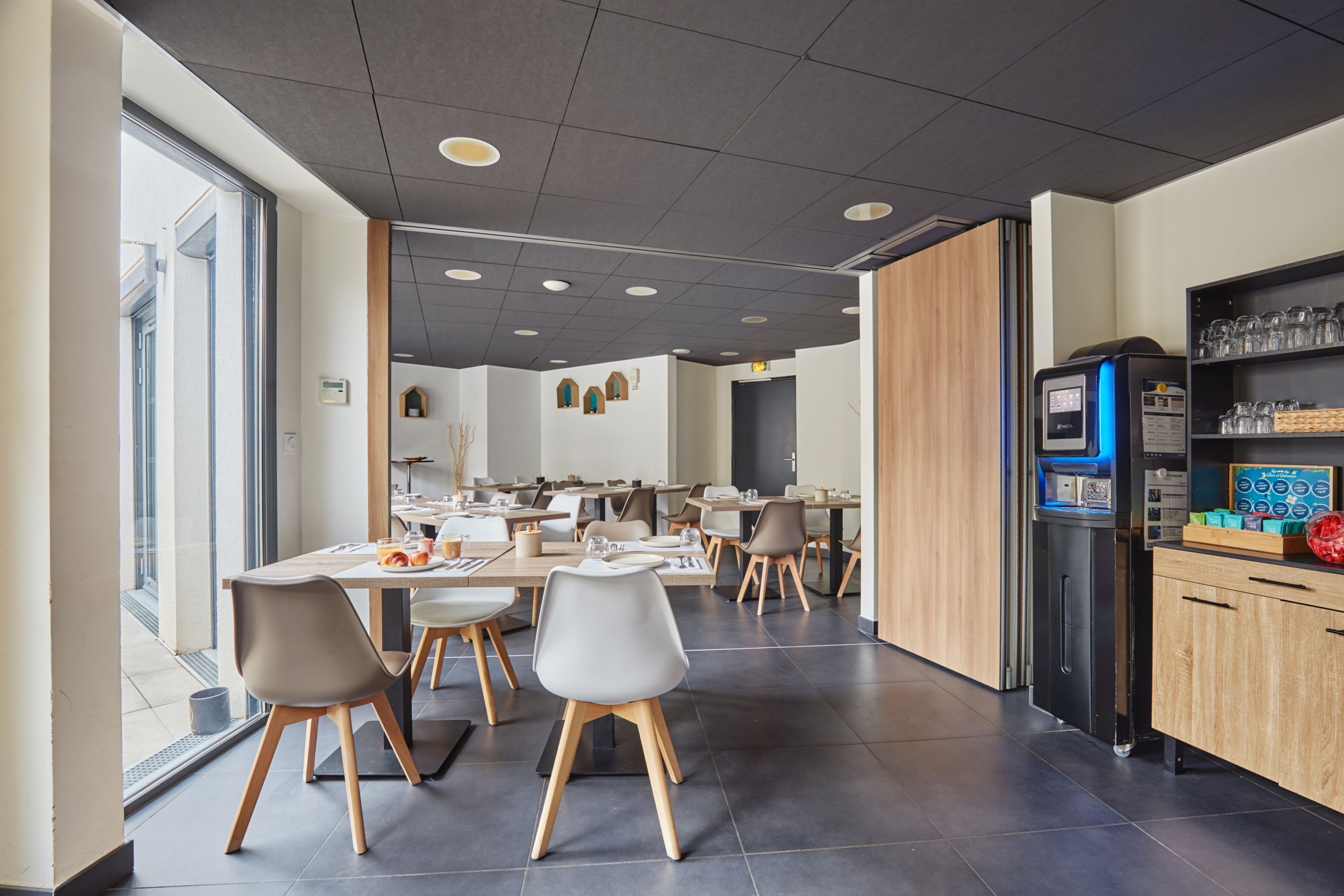 A modern dining area with tables and chairs, a vending machine, and a view of the outside.