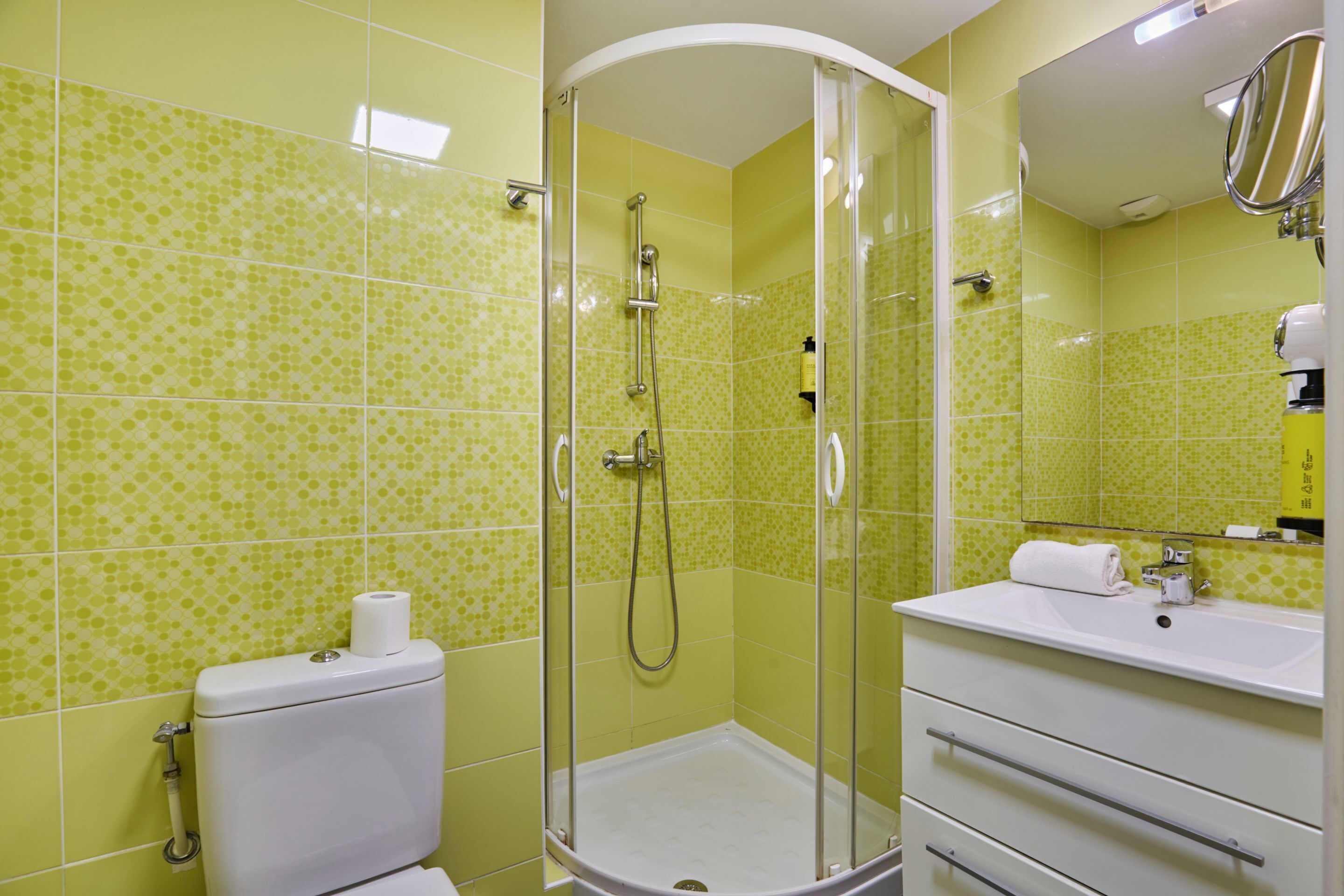 A bathroom with a toilet, a glass-enclosed shower, and a sink with a mirror.