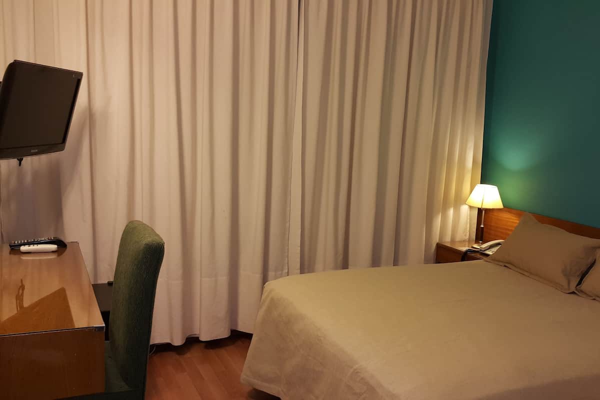 A hotel room with a bed, a chair, a TV, a lamp, and curtains.