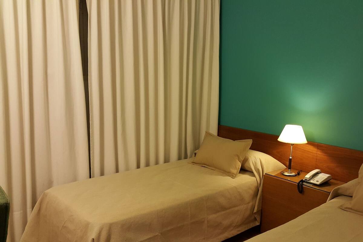 A hotel room with two single beds, a nightstand with a lamp, and a telephone.