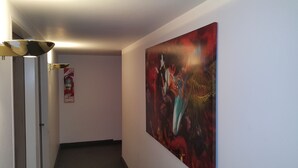 A hallway with a large abstract painting on the wall, a fire extinguisher, and a door with a light fixture. - Hotel Avenida (Buenos Aires)