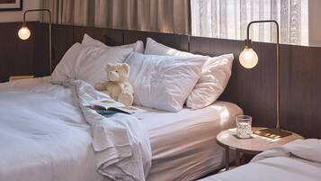 A neatly made bed with white linens, a teddy bear, and a book, with a bedside table holding a glass and a candle.